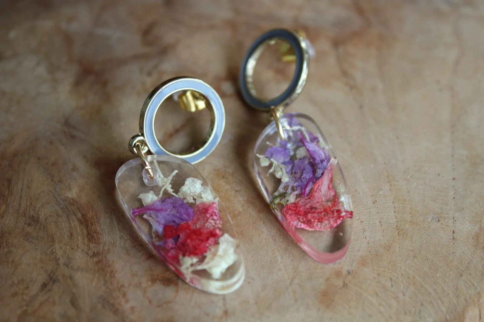 Paire de boucles d'oreilles à anneau gris et résine contenant des pétales séchés, posée sur du bois.