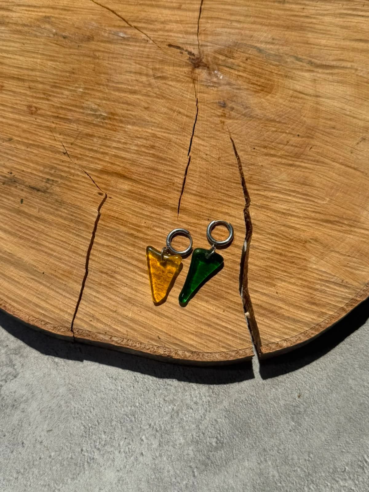 Main tenant les boucles d'oreilles en verre translucide jaune et vert devant une plante.