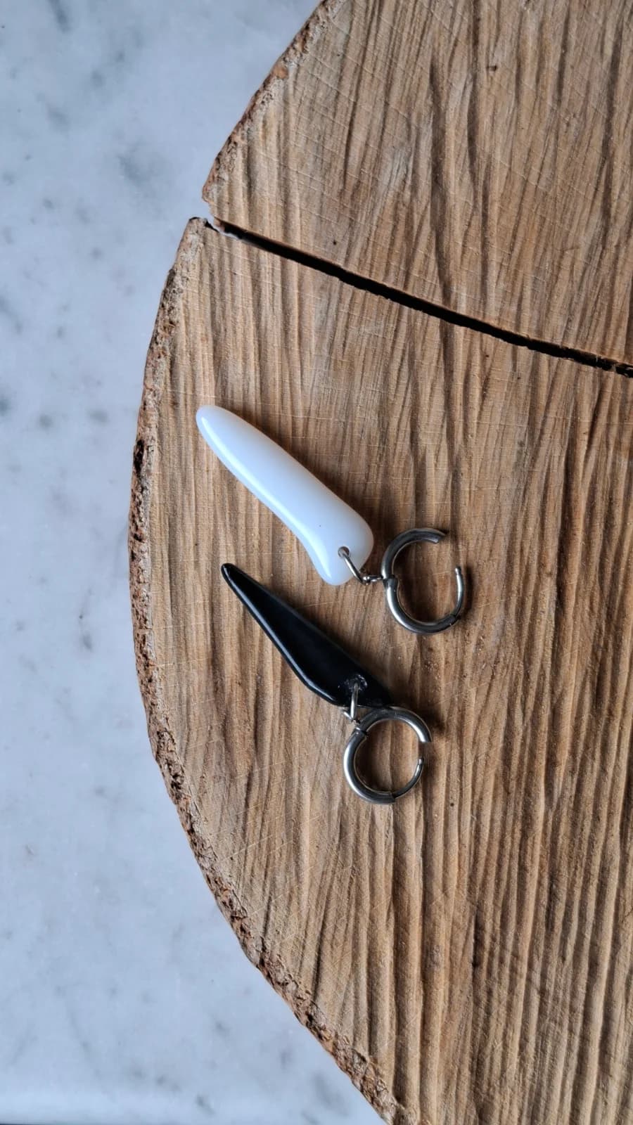 Boucles d’oreilles asymétriques en verre noir et blanc sur anneaux métalliques, posées sur un socle en bois.