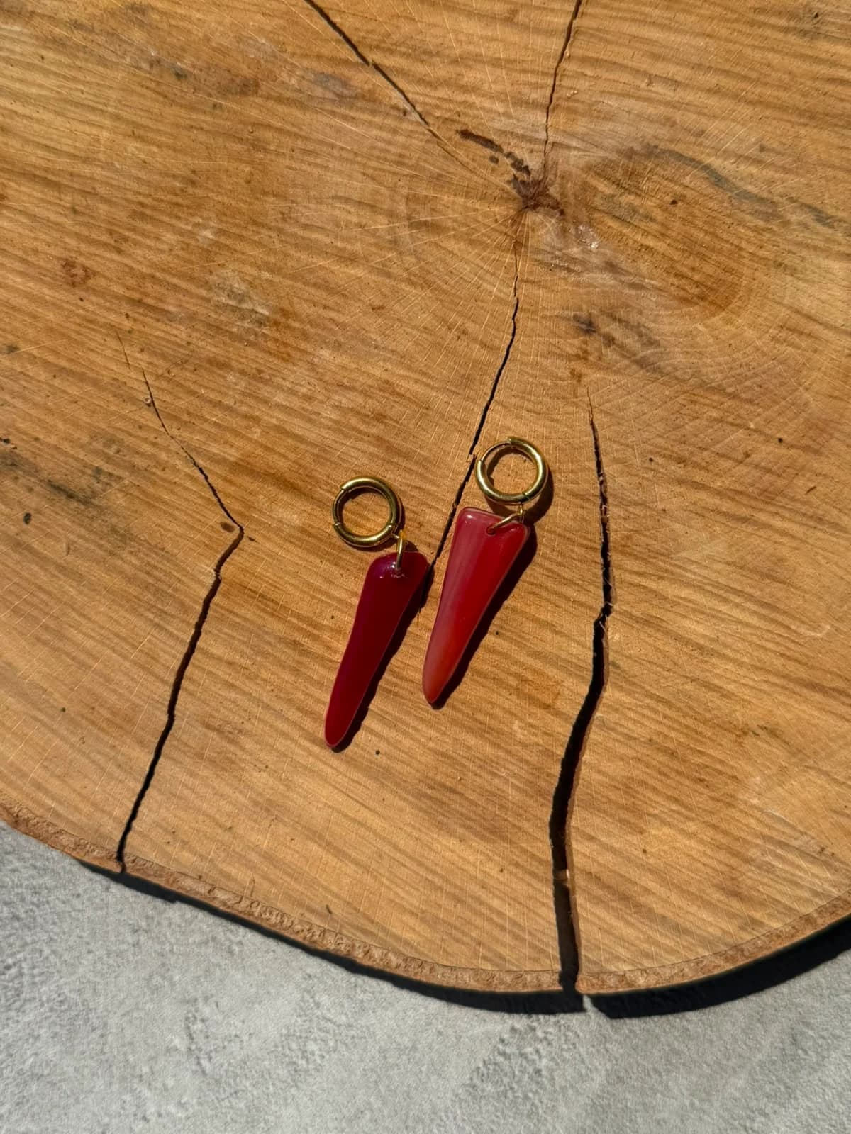 Boucles d'oreilles pendantes en verre rouge et dormeuses dorées posées sur un rondin de bois.