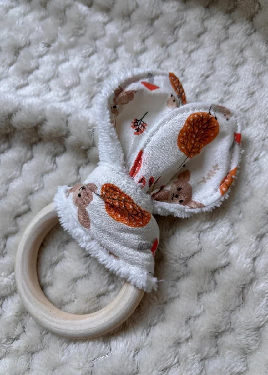 Anneau de dentition en bois orné d'oreilles en tissu à motifs d'automne posé sur un tissu écru.