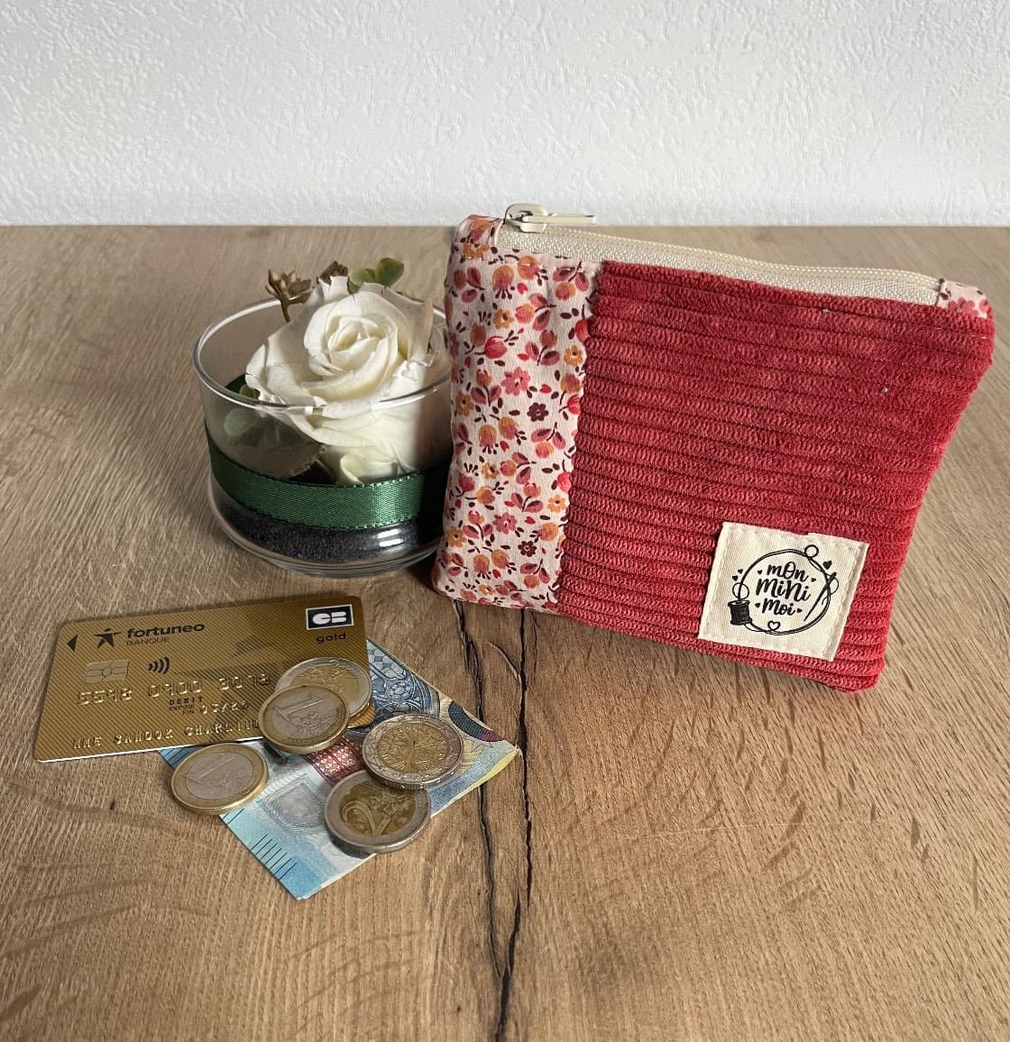 Porte-monnaie plat en velours côtelé rose framboise et tissu fleuri posé près de monnaie.