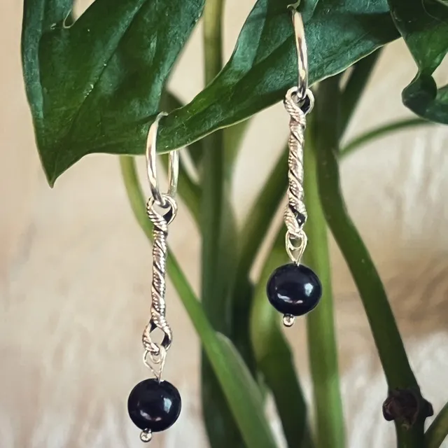 Gros plan sur les créoles pendantes argentées avec pendentif torsadé et perles d'eau douce sombres.