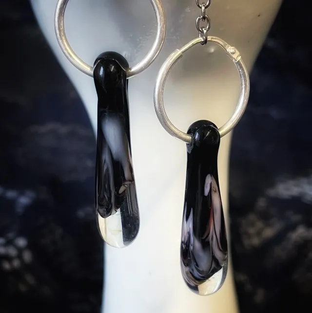Gros plan sur les pendentifs gouttes en verre filé noir marbré blanc montés sur créoles argentées.
