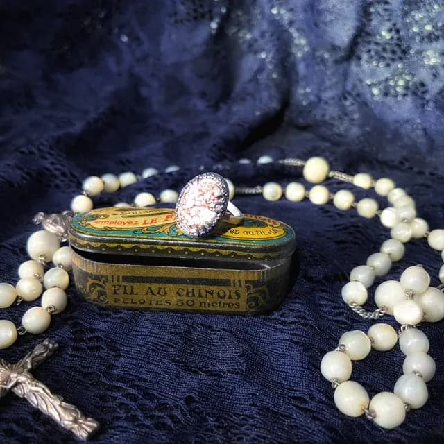 Bague avec cabochon ovale disposée sur une boîte ancienne entourée d'un chapelet en perles claires