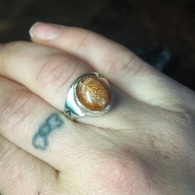 Chevalière en argent sertie d'une pierre de soleil orangée portée au doigt.