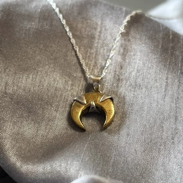 Collier avec pendentif croissant de lune doré posé sur un tissu satiné gris.