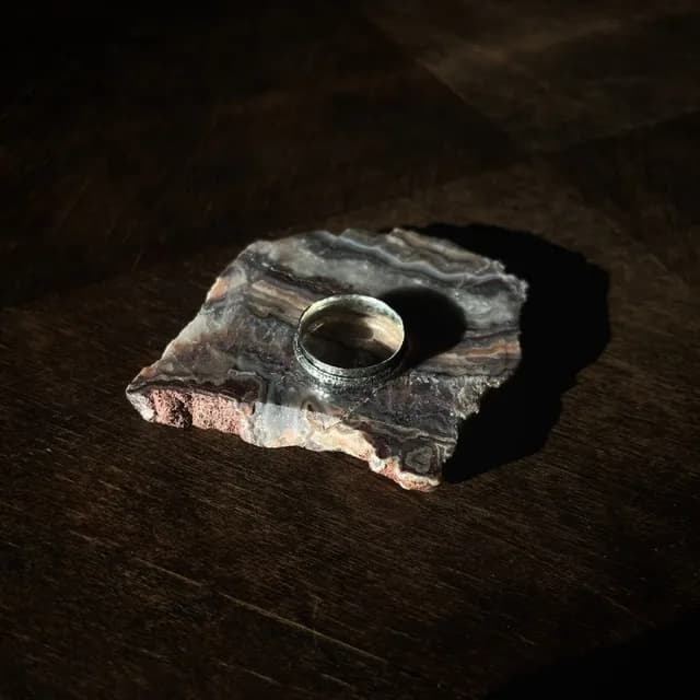 Bague en métal argenté posée sur une pierre minérale avec jeu d'ombre et lumière.