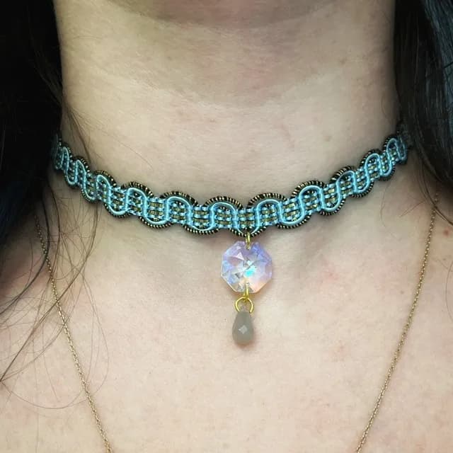 Gros plan sur le pendentif irisé à facettes et la perle d'agate grise du ras de cou