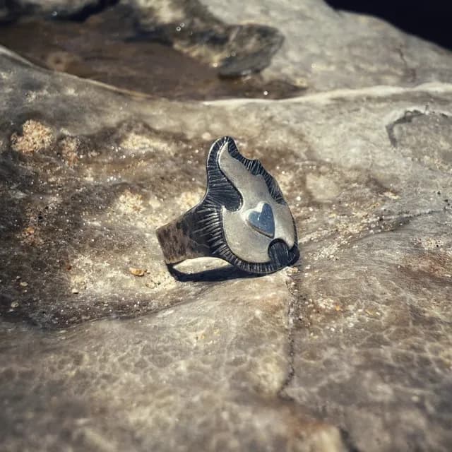 Vue de trois-quarts de la bague en argent ornée d'une flamme avec cœur central sur fond minéral.