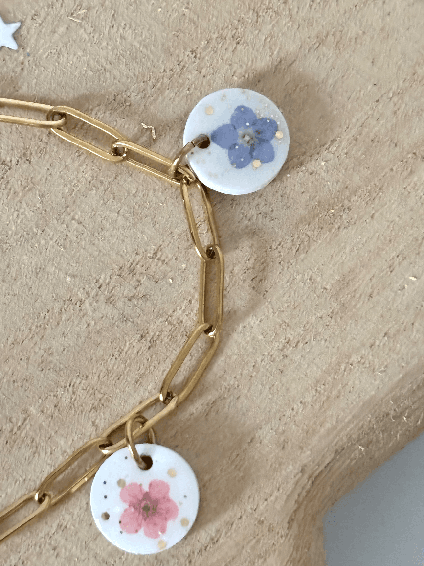 Gros plan sur la chaîne dorée et deux médaillons ornés d'une fleur bleue et d'une fleur rose.