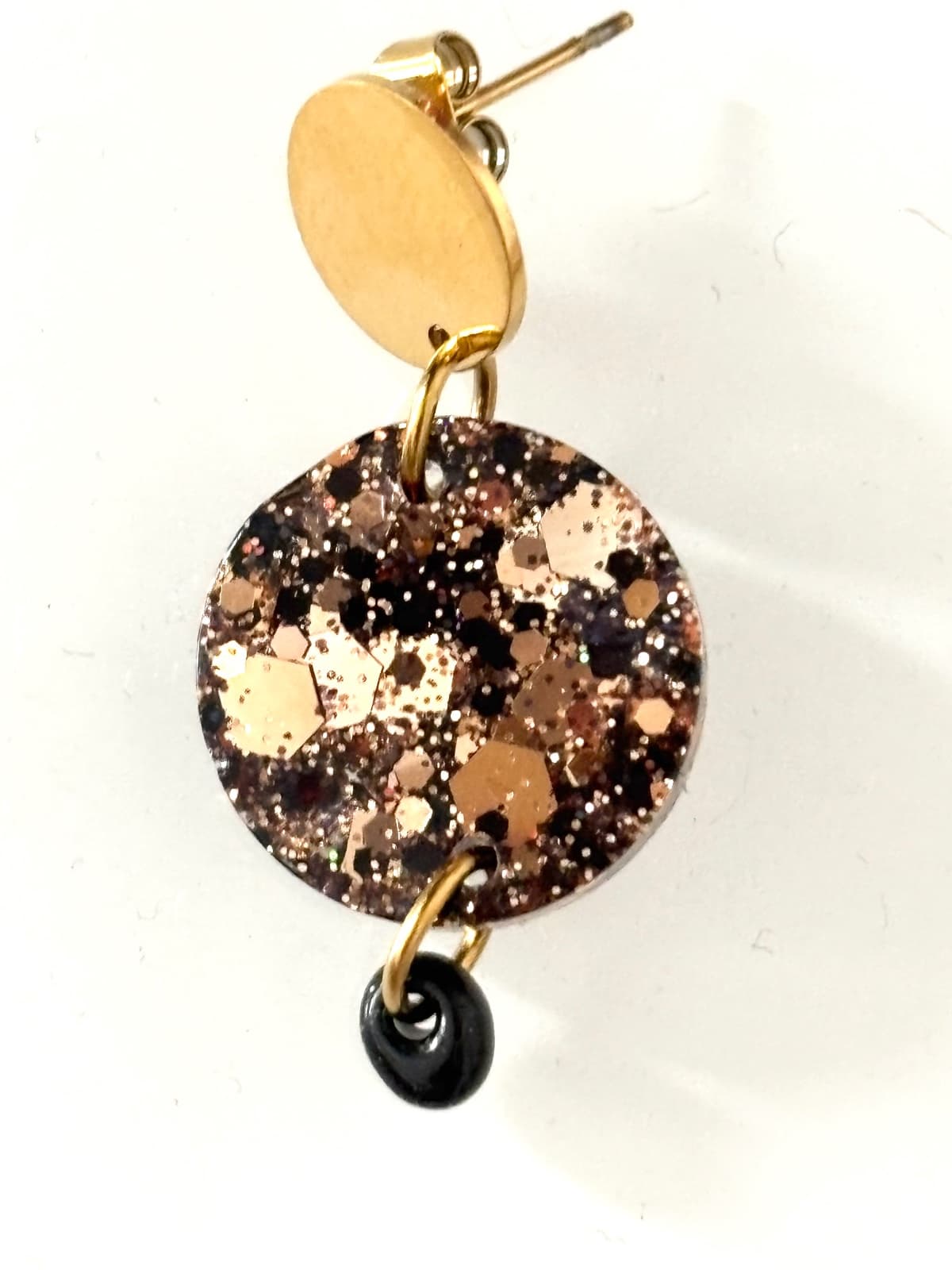 Gros plan sur une boucle d'oreille ronde dorée avec médaillon à paillettes noires et dorées