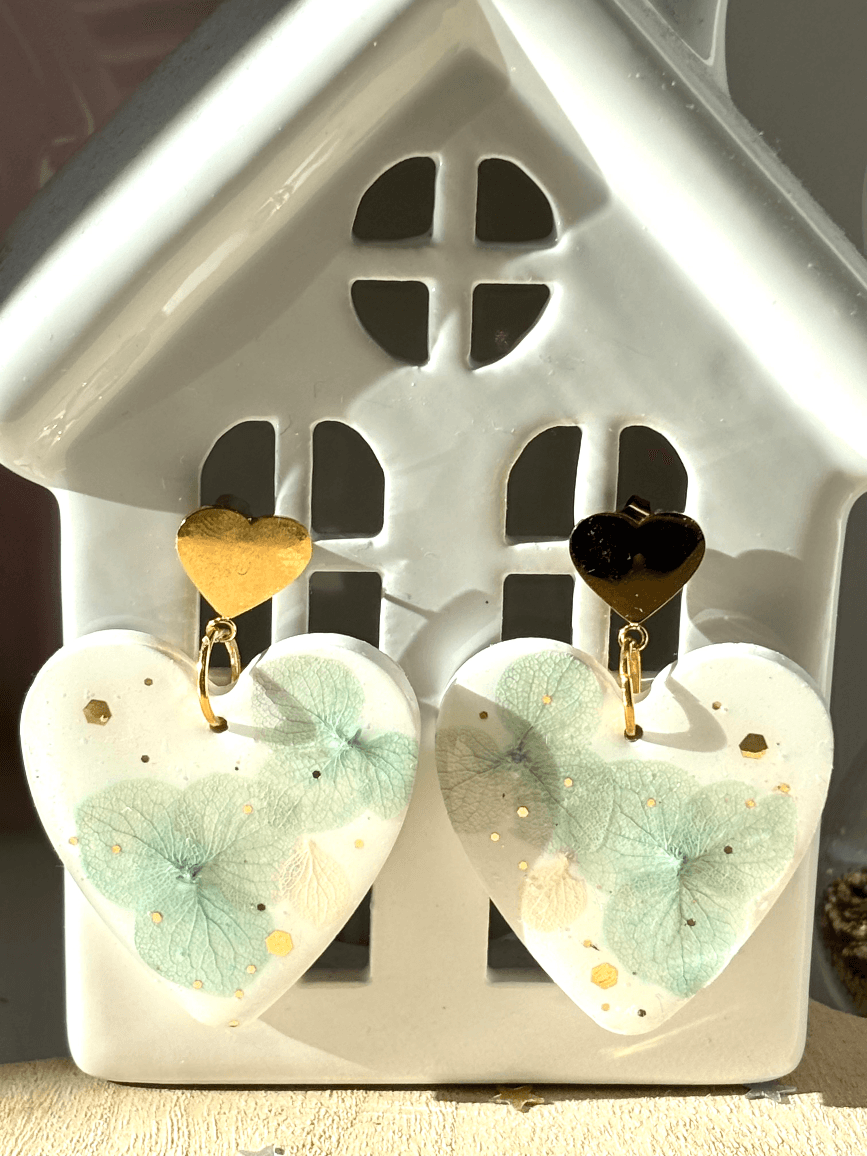 Boucles d'oreilles pendantes cœur en résine blanche avec inclusions florales posées à plat.
