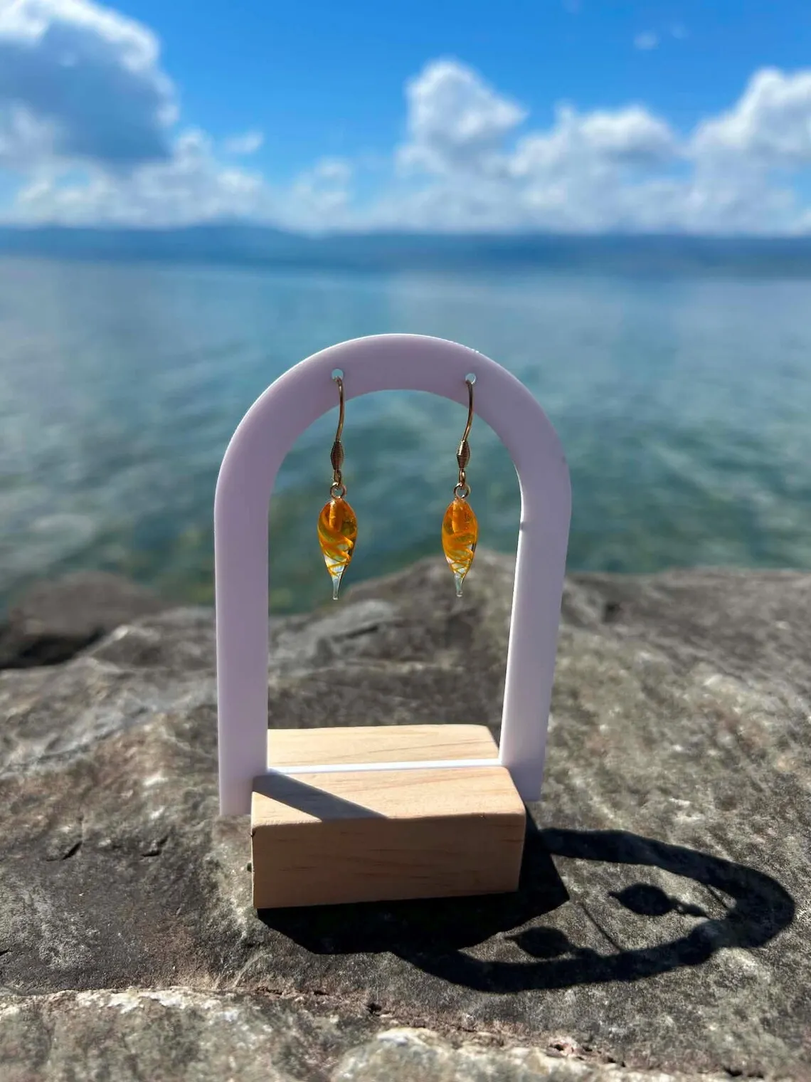 Paire de boucles d'oreilles pendantes en verre filé orange torsadé sur un présentoir arche blanc.
