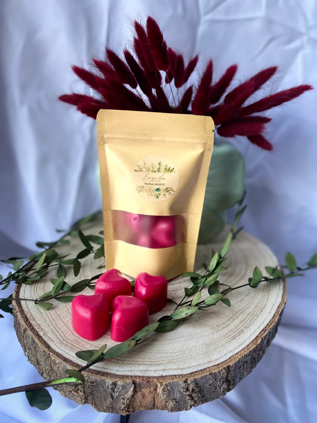 Quatre fondants roses en forme de cœur et leur sachet kraft sur un rondin de bois décoré.